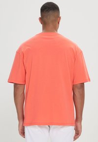 T-shirt in cotone corallo con vestibilità rilassata, maniche corte e design semplice. Presenta un collo a giro e orlo dritto in vita.