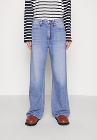 Lichtblauwe wijde jeans hebben een klassieke five-pocket stijl en zichtbare stiksels. Gecombineerd met een gestreept zwart-wit shirt met lange mouwen.