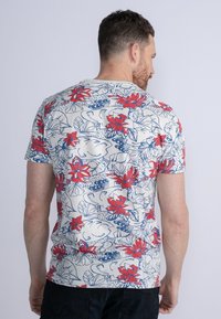 Camisa de manga corta de tejido ligero con un patrón floral que presenta flores rojas y hojas azules sobre un fondo crema.
