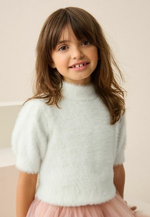 Flauschiger weißer Pullover mit hohem Kragen und kurzen Ärmeln, kombiniert mit einem hellrosafarbenen Tüllrock, zeichnet sich durch eine weiche Textur und eine lockere Passform aus.