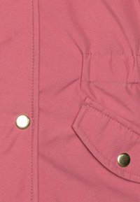 Veste rose avec une texture lisse, boutons-pression dorés et une poche plaquée. Présente des détails de couture le long des coutures.