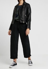 Černá kožená motorkářská bunda s prošívanými detaily na ramenou, spárovaná s černými džínovými kalhotami s vysokým pasem a klasickými černobílými teniskami.