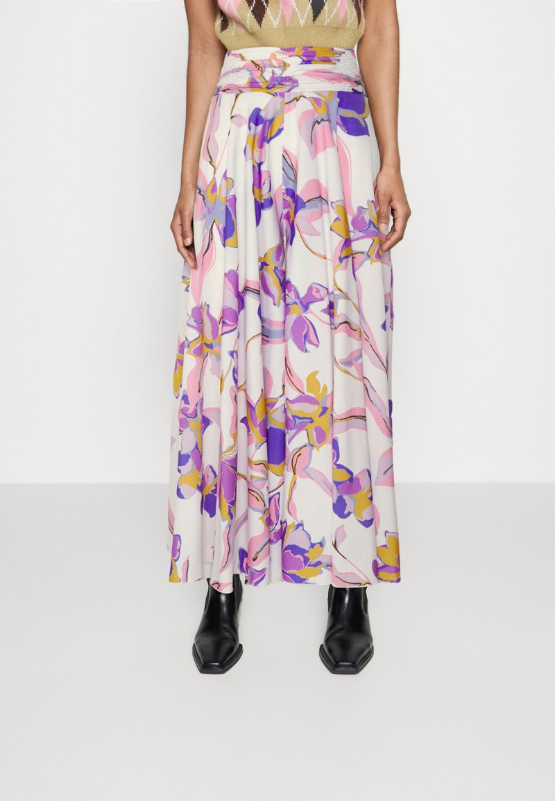 Ziedu maksi svārki baltā audumā ar purpura, rozā un dzeltenām apdrukām, augstu jostasvietu un plūstošu dizainu, savienoti ar melniem potīšu zābakiem.