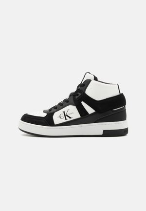 Fekete és fehér bőrből készült magas szárú sneaker, velúr részletekkel, strukturált dizájnnal, kerek orral és fehér gumitalppal. A logó részlet látható.
