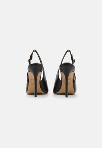 Chaussures à talons hauts noires à brides arrière en cuir lisse, dotées d'un talon fin et d'un design minimaliste avec un détail en boucle dorée.