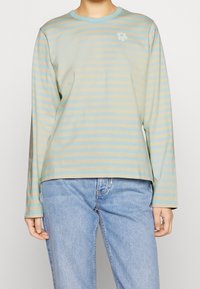 Lättvikts långärmad skjorta i pastellblå och beige horisontella ränder, med en liten blommönster på bröstet. Mjuk, avslappnad passform.