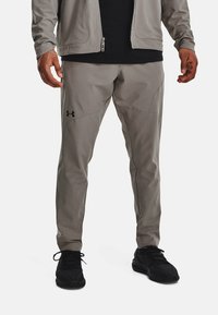 Grå träningbyxor med smal passform, med svarta sömmar och detaljer, samt en Under Armour-logotyp på vänster lår.