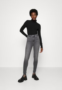 Svart ribbestrikket turtleneck-genser kombinert med høy midje grå skinny jeans og svarte blokkhæl sko. Enkel, tettsittende design.