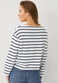 Weißes Langarmhemd mit navyblauen horizontalen Streifen, rundem Ausschnitt und lockerer Passform. Der Stoff wirkt weich mit einer subtilen Textur.