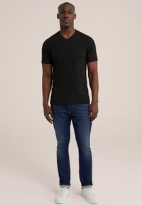 Tricou negru cu decolteu în V, mâneci scurte, design ajustat, asortat cu blugi albaștri și adidași albi, țesătură texturată, linii curate.