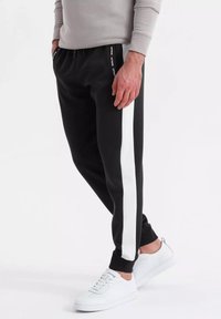 Zwarte joggerbroek met witte zijstrepen, gemaakt van zachte stof. Voorzien van een elastische tailleband en ribgebreide boorden, gecombineerd met witte sneakers.