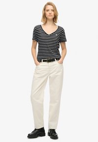 Stribet marineblå og hvid V-hals t-shirt kombineret med cremefarvede bukser, sort bælte og sorte snørebåndsstøvler. Simpelt og afslappet outfit.