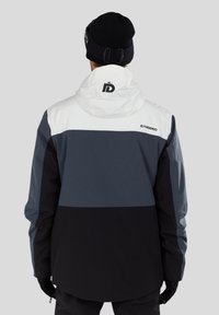 Farbenfroh blockierte Jacke mit Abschnitten in Schwarz, Grau und Weiß, mit Kapuze und Logo auf dem Rücken. Glatte Textur und funktionales Design.