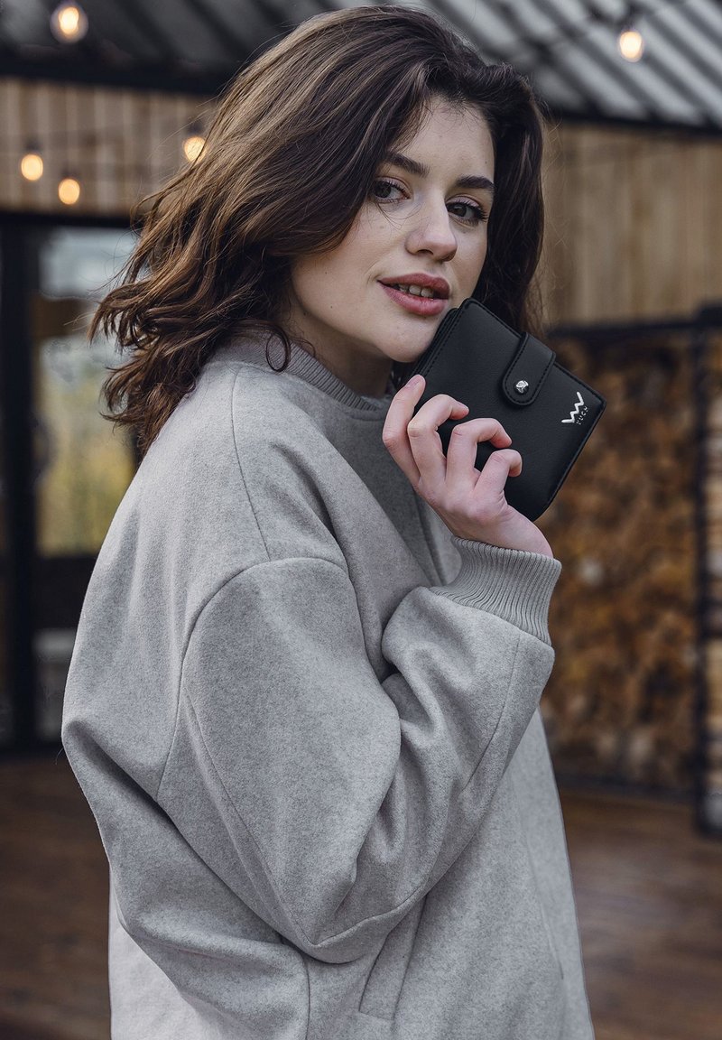 Black leather wallet with a snap closure, held in a hand, paired with a light gray fleece sweatshirt featuring ribbed cuffs.