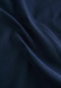 Dunkelblauem Stoff mit glatter Textur und subtiler Schattierung, der sanfte Falten aufweist, die die Flexibilität und eine leichte Beschaffenheit anzeigen.
