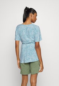 Top com estampado floral em azul e branco, apresentando mangas curtas e cintura ajustada. Combinado com calções verdes claros, exibindo um ajuste descontraído.