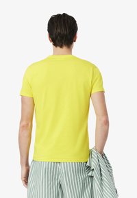 Geel katoenen t-shirt met korte mouwen en een klassieke ronde hals, met een gladde textuur en een aansluitend ontwerp; gedragen met groen-witte gestreepte shorts.