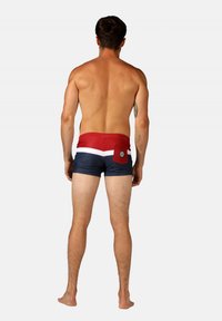 Un short de bain avec des blocs de couleur rouge, blanc et bleu marine, dot é d'une poche arrière et d'un détail de logo. Fabriqué en matériau lisse et extensible.