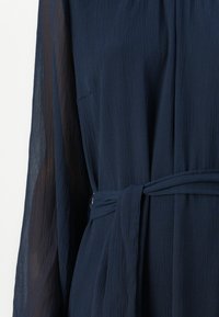 Ναυτικό μπλε φόρεμα με υφή. Διαθέτει μακριές διαφανείς μανίκες και ζώνη στο τσάκι στο μέσο. Μαλακή πτώση και άνετη εφαρμογή.