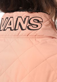 Prošívaná světle růžová bunda s vysokým límcem, zdobená černým vyšívaným logem "VANS" a hladkou, lesklou texturou.