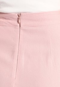 Pantalons en tissu rose avec une texture lisse, une fermeture éclair à l'arrière et des détails de couture le long de la taille.