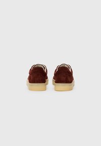 Brown suede shoes with a low profile and cushioned beige sole, featuring a smooth rounded back and minimal stitching detail.