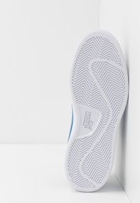 Modrá sportovní bota s texturovanou bílou gumovou podrážkou se zigzagovým vzorem a značkováním Puma. Boční profil ukazuje elegantní, aerodynamický design.