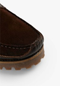 Zapato de cuero marrón con parte superior de gamuza, puntera reforzada, costuras en contraste y suela de goma texturizada con tacos visibles.