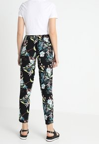 Pantalon noir à motif floral vibrant multicolore, coupe slim, taille élastique et longueur cheville.
