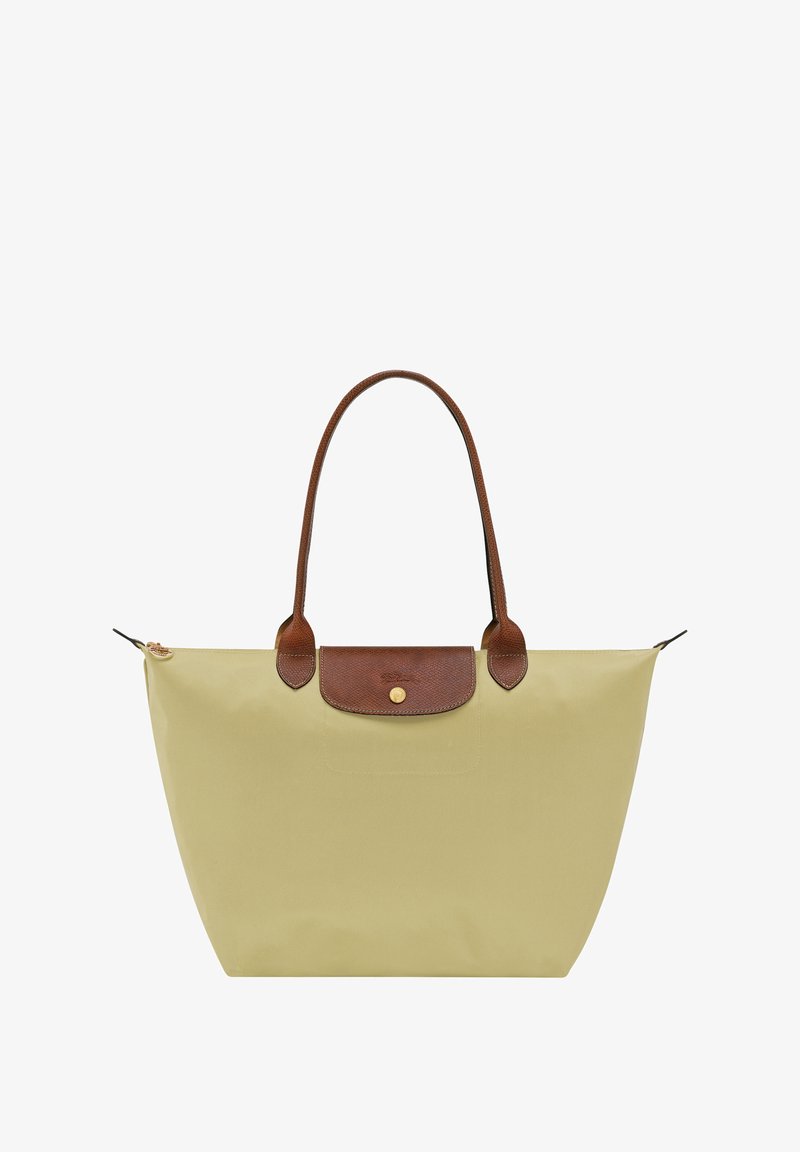 Tote bag in light yellow nylon with brown leather handles and a top flap closure featuring a gold logo. Smooth, water-resistant texture.