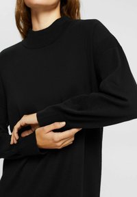 Pullover nero a maglia con collo alto, vestibilità rilassata e dettagli a coste sulle maniche. Texture morbida, maniche lunghe e design minimal.
