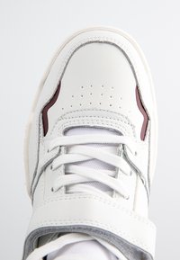 Witte sportschoen met een leren bovenwerk, met mesh accenten, perforaties op de neus en een contrasterende bordeauxkleurige zijdetail.