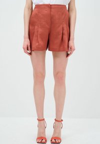 Pantaloni shorts in lino color ruggine con pieghe e vita alta. Tessuto morbido, orlo risvoltato e design sartoriale. Abbinati a sandali con cinturini coordinati.