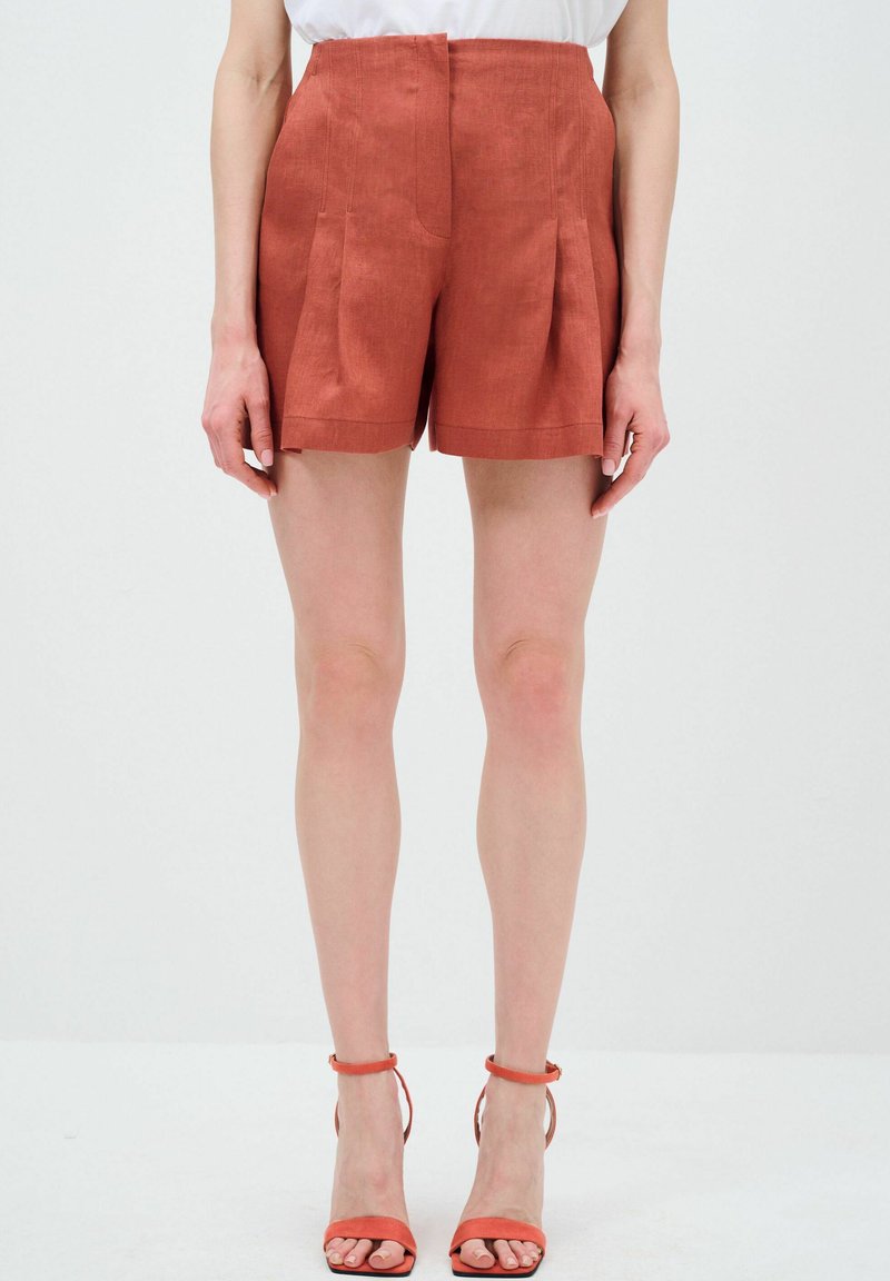 Roodkleurige linnen shorts met plooien en een hoge taille. Gladde textuur, omgeslagen zoom en een op maat gemaakt ontwerp. Gecombineerd met bijpassende sandalen met banden.