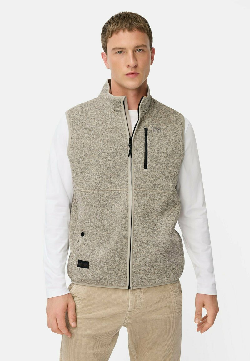 Grau fleece Weste mit hohem Kragen, Vorderreißverschluss und schwarzem Reißverschlussfach. Getragen über einem weißen Langarmshirt und beigen Hosen.