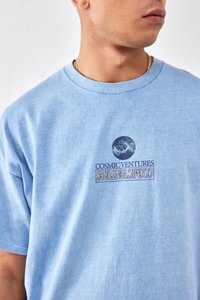 Light blue cotton t-shirt with short sleeves, featuring a printed logo and graphic on the front. Ribbed crew neck. Simple design.