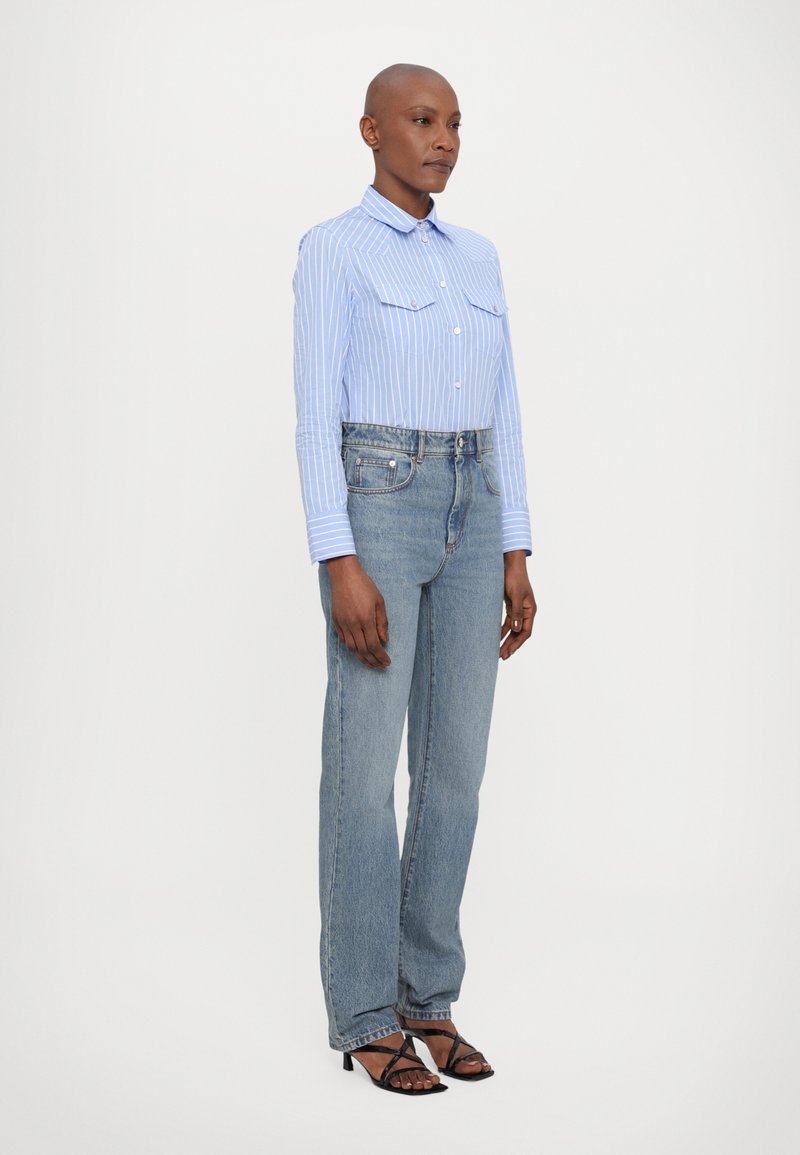 Light blue striped button-up shirt with two chest pockets, paired with high-waisted light blue jeans and black strappy heeled sandals.