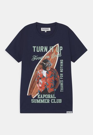 Granatowa koszulka z nadrukiem szympansa w okularach przeciwsłonecznych i czerwonej tropikalnej koszuli, stojącego przed deską surfingową z tekstem o tematyce letniej.