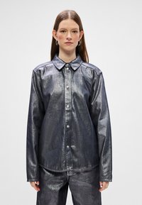 Casaco metálico azul-escuro com colarinho clássico, mangas longas e fecho com botão, apresentando uma textura suave e um brilho subtil.