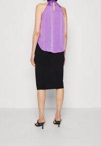 Top halter in raso viola con dettaglio a chiave sul retro, abbinato a una gonna a tubino nera aderente. Sandali neri con tacco completano il look.