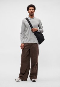 Γκρι πόλο πουκάμισο μακρυμάνικο με φερμουάρ στον γιακά, καφέ κορδωτά παντελόνια με φαρδιά μπατζάκια και μαύρη τσάντα χιαστί. Τα παπούτσια είναι ασημί με μαύρες λεπτομέρειες.