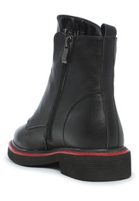 Bottine en cuir noir avec une fermeture éclair sur le côté, bout rond et semelle en caoutchouc texturée avec un accent rouge autour de la base.