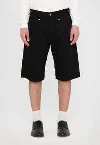Shorts din denim negru cu un croi drept, având cinci buzunare și accesorii din argint, asortați cu șosete albe și pantofi negri.