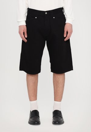 Black denim shorts with a straight cut, featuring five pockets and silver hardware, paired with white socks and black shoes.