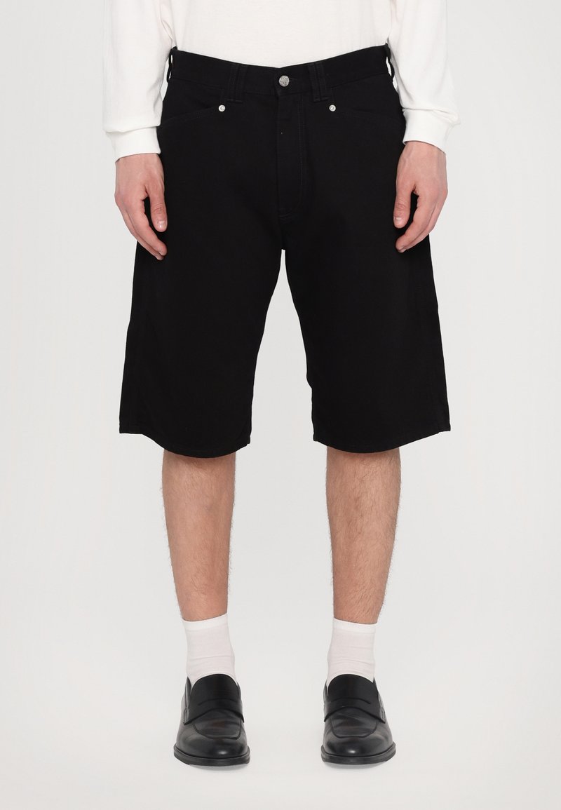 Shorts din denim negru cu un croi drept, având cinci buzunare și accesorii din argint, asortați cu șosete albe și pantofi negri.