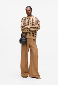 Beige mønstrete genser med svarte geometriske design, kombinert med beige vide bukser og svart teksturert veske. Leopardmønstrede sko.