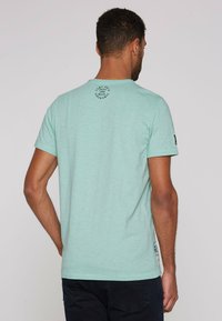Camiseta de manga corta verde menta con escote redondo y detalle de logotipo de goma en la parte superior de la espalda, fabricada con una tela suave y texturizada.