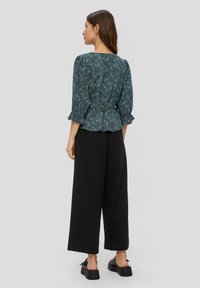 Floral bedrucktes Peplum-Top mit dreiviertellangen Rüschensägen, kombiniert mit weiten schwarzen Hosen und Plateau-Sandalen. Glatte Stofftextur.