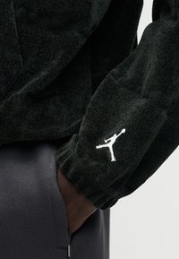 Μαύρο φούτερ με υφή και λευκό κεντημένο λογότυπο στο μανίκι. Διαθέτει δομημένο σχεδιασμό και παχύ υλικό ύφασμα.