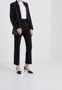 Completo nera su misura con giacca cropped, camicia bianca a maniche lunghe e pantaloni neri aderenti. Abbinato a tacchi neri a punta e una piccola borsa.